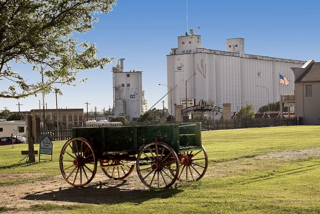 White concrete grain elevators behind a restored wooden wagon in Dodge City, Kansas